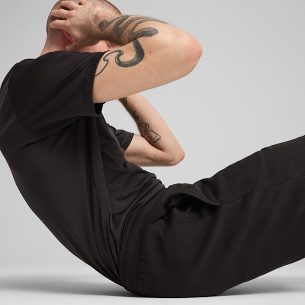 On grey, a tattooed model in black sportswear does crunches, hands behind their head.